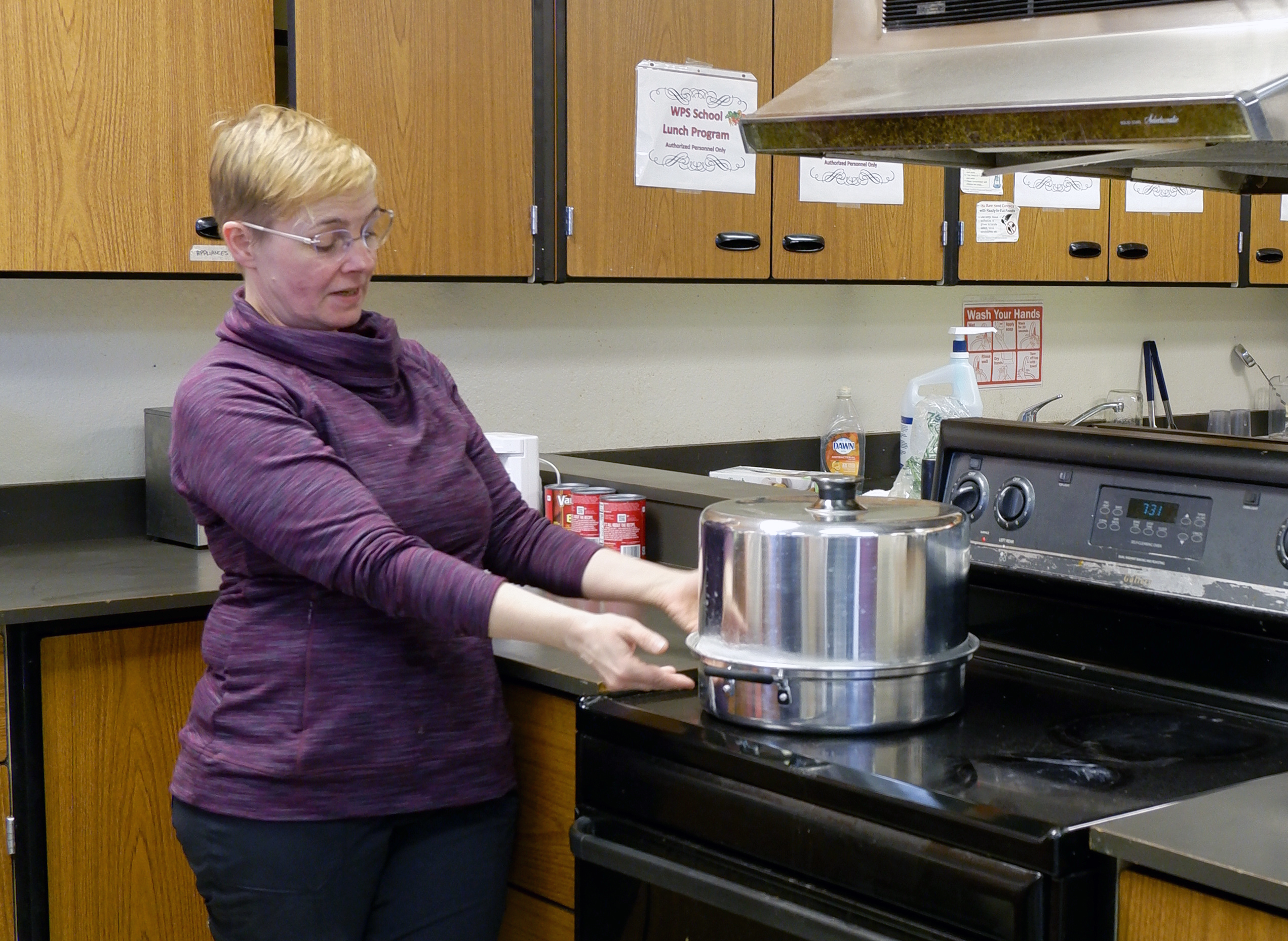 A woman gestures today a piece of food preservation equipment on a stove in a community kitchen.