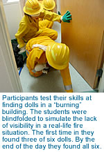 [Participants test their skills at finding dolls in a 'burning' building.]