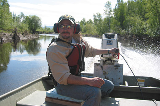 Curtis Knight guides a motorboat down the Kanuti River on a sunny day.