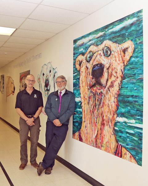 Paul McCarthy photo.  Alaska Nanooks swimming coach Scott Lemley, left, and UAF College of Liberal Arts Dean Todd Sherman pose in a hallway filled with Sherman's art in the Patty Center.