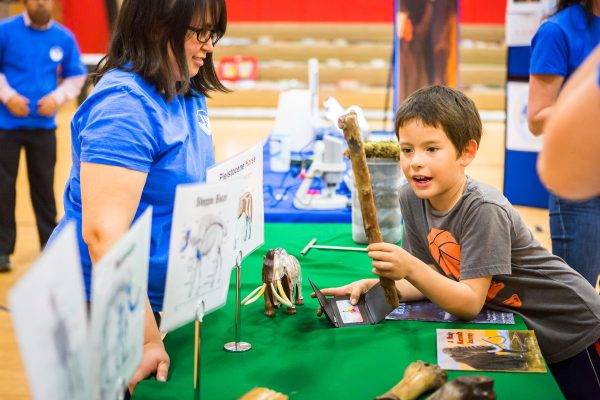 UAF photo by JR Ancheta. Margaret Cysewski, an outreach educator with the UAF Geophysical Institute, talks to a Tanana boy as he examines a 30,000-year-old willow stick from the Fox permafrost tunnel in 2016. The institute has brought its permafrost presentations to Tanana and 36 other Alaska villages and towns as part of a National Science Foundation-funded education project.