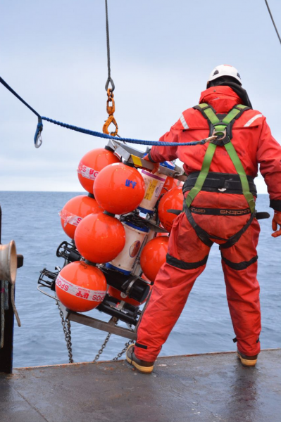 Photo courtesy of the Chukchi Ecosystem Observatory.  A ship crew member holds a Chukchi Sea mooring that contains floatation and housing for an acoustic zooplankton and fish profiler and biogeochemical sensors.