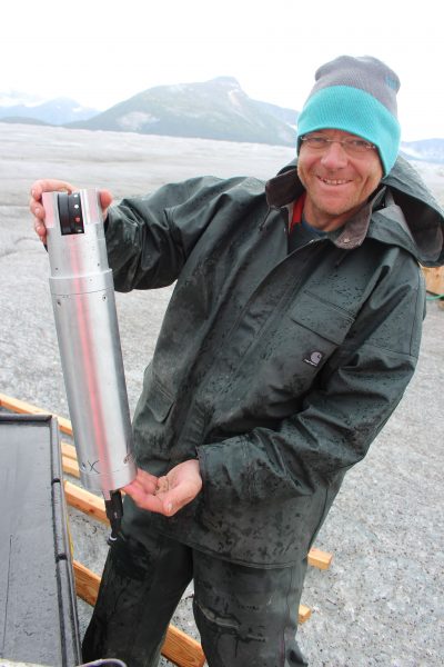 Photo courtesy of Martin Truffer.  Martin Truffer, UAF professor, stands on Taku Glacier in Southeast Alaska while holding a device that helps analyze how ice and till move at a glacier's base.