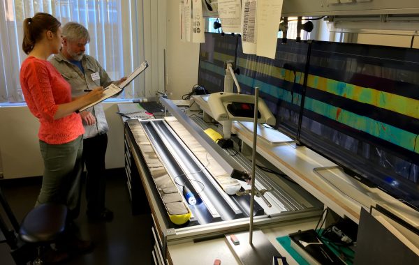 Photo by Kevin Kurtz. Michael Whalen, of UAF's Geophysical Institute, and Elise Chenot, a French doctoral student, describe a sediment core from the Chicxulub impact crater at the IODP Bremen Core Repository in Germany. The screens have images from CT scans of the core.