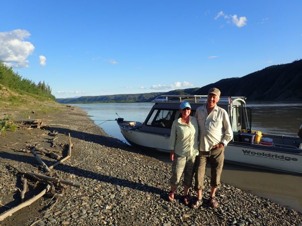 Photo by Ned Rozell. Chris Florian and her husband Skip Ambrose stand next to the Yukon River across from cliffs where peregrine falcons nest.