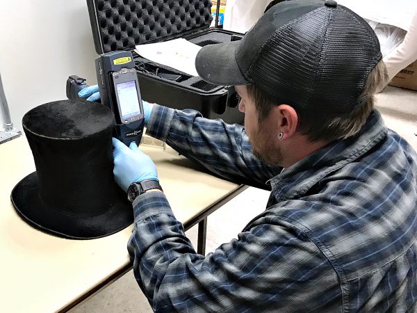 Photo by Kelly McCartney. Nathan Graham, a UAF graduate student, uses an X–ray fluorescence spectrometer to test for mercury in an antique felted top hat.