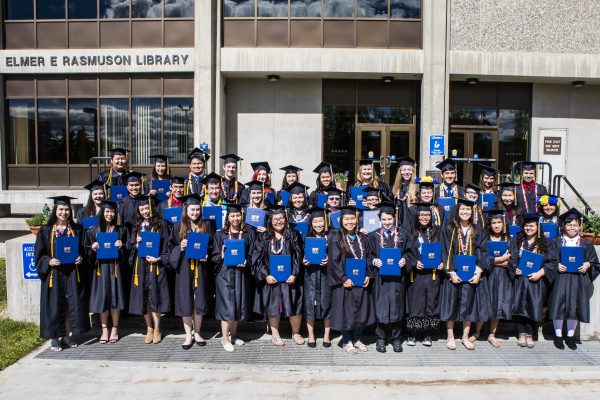 UAF photo by JR Ancheta. Forty Alaska Native and rural high school students hold their Rural Alaska Honors Institute diplomas following the 2018 cap and gown ceremony at the University of Alaska Fairbanks.