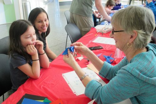 UA Museum of the North photo. Volunteer Judy Ferri folds origami cranes with two visitors during Birds Family Day.