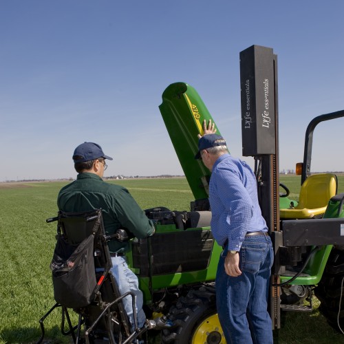 Photo courtesy of the National AgrAbility Project. A farmer with a disability meets with an occupational therapist and uses a Superstand wheelchair to work on a tractor.