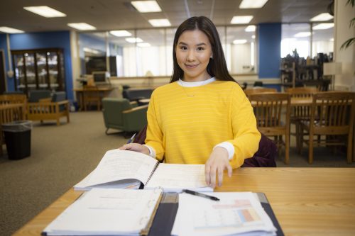 Student with long brown hair and yellow shirt studying