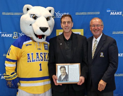 Photo by Paul McCarthy. Scott Roselius holds his award as he stands between UAF mascot Nanook and athletic Director Gary Gray during his induction into the Nanook Hall of Fame in 2016, when he was given the Alumni Achievement Award for Community Support.