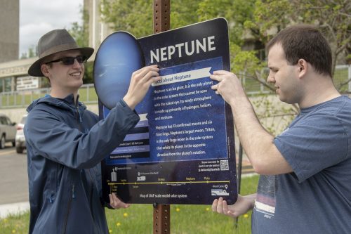 UAF Geophysical Institute photo by Sean Tevebaugh. Evans Callis, left, and Devon Gerstenfield, both with the UAF Society of Physics Students, install signs along Yukon Drive to create the Planet Walk in May 2019.