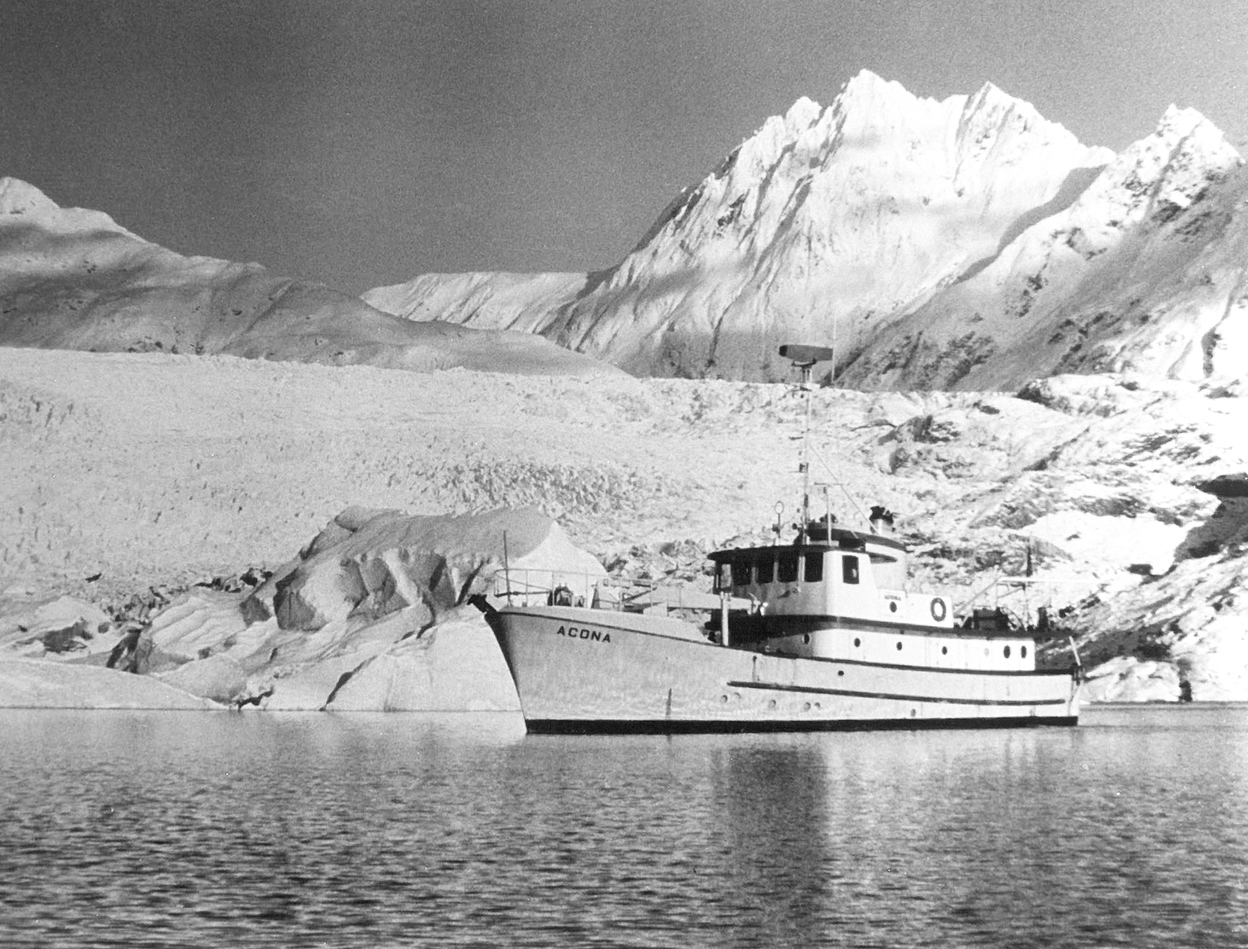 Photo courtesy of the Seward Marine Center. Acona, the first research ship homeported at SMC, pauses near a glacier. Acona was moved to Seward from Douglas, Alaska, in 1970.