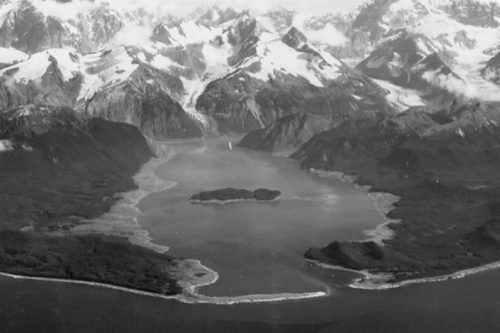 Photo by Donald Miller, U.S. Geological Survey. An earthquake-triggered tsunami stripped vegetation from the hills and mountains above Lituya Bay in 1958. The treeless areas are visible as lighter ground surrounding the bay in this photograph taken shortly after the event.