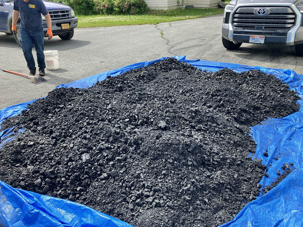 A mound of black, charcoal-looking material is piled on a blue tarp.