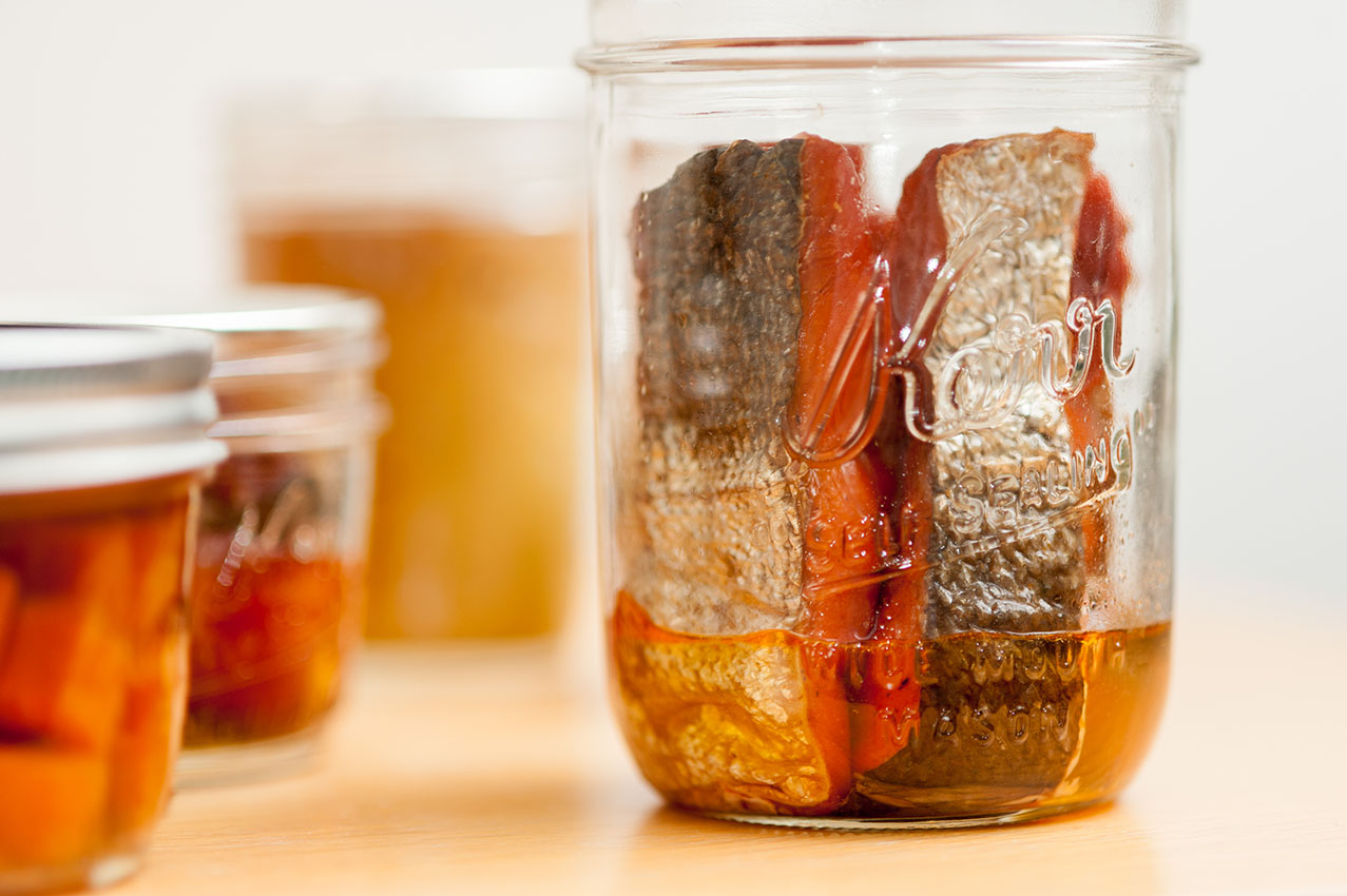 Salmon strips are placed in a clear canning jar prior to preservation.