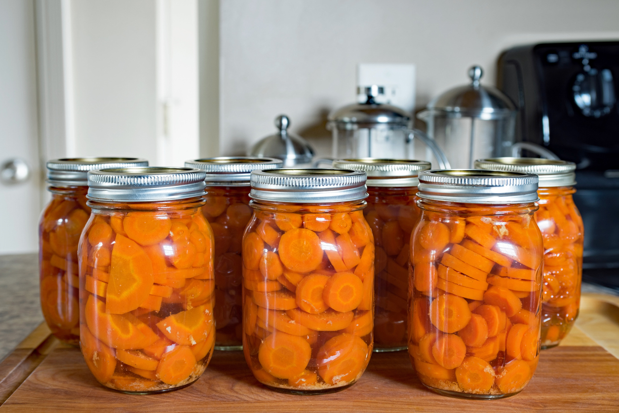 Canning jars full of bright orange carrot slices on a kitchen counter
