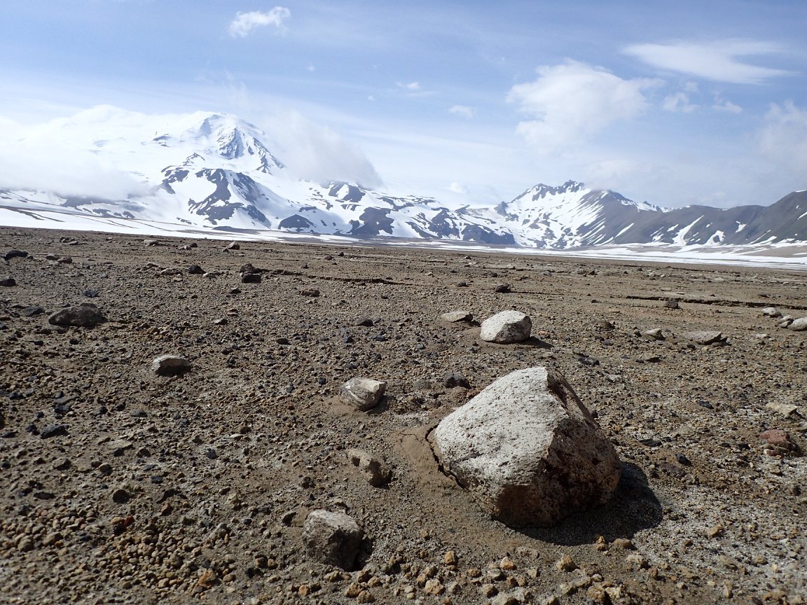 Boulders sit on a plain of gravel with snowy mountains in the background.