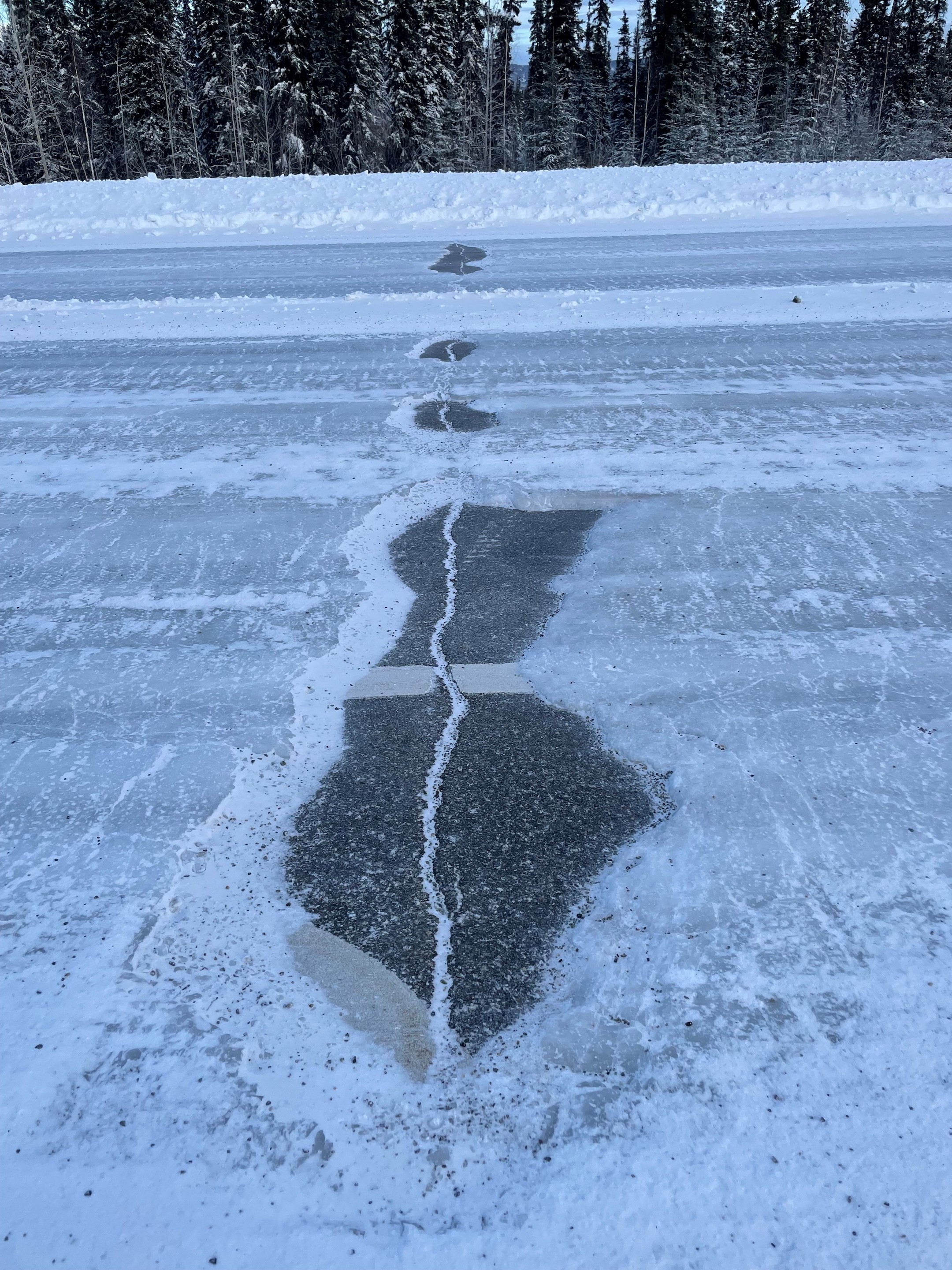 A crack in a snowy road is free of ice