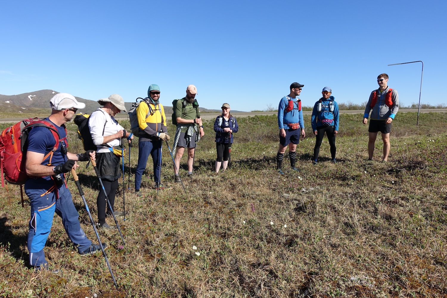 Eight people in hiking gear stand on tundra under a blue sky.