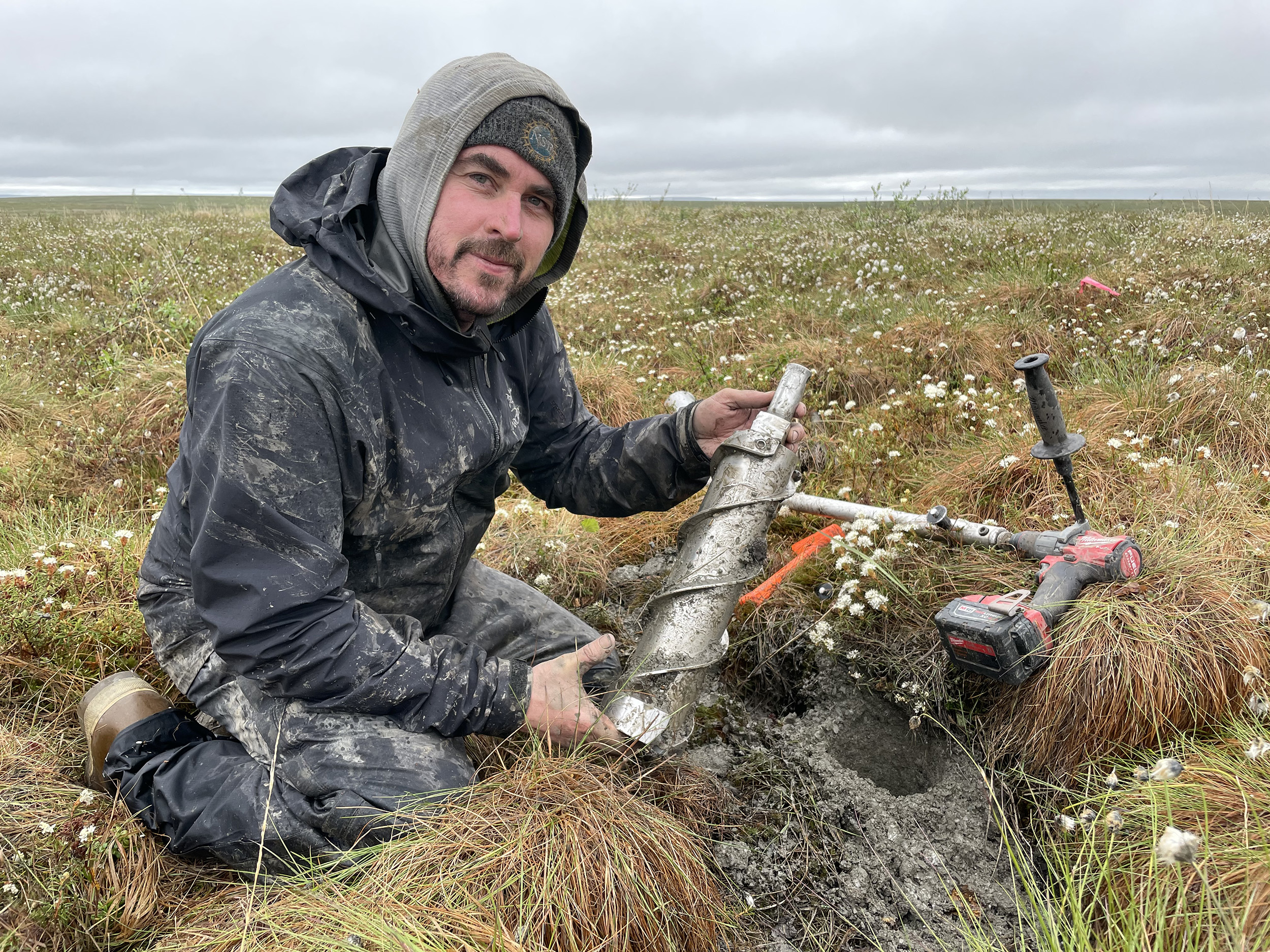 A man kneels with a coring device on the tundra