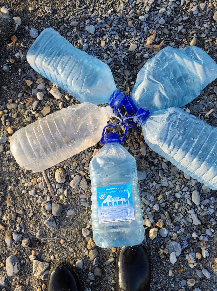 Several clear plastic bottles are arranged in a star circle on a gravel beach.