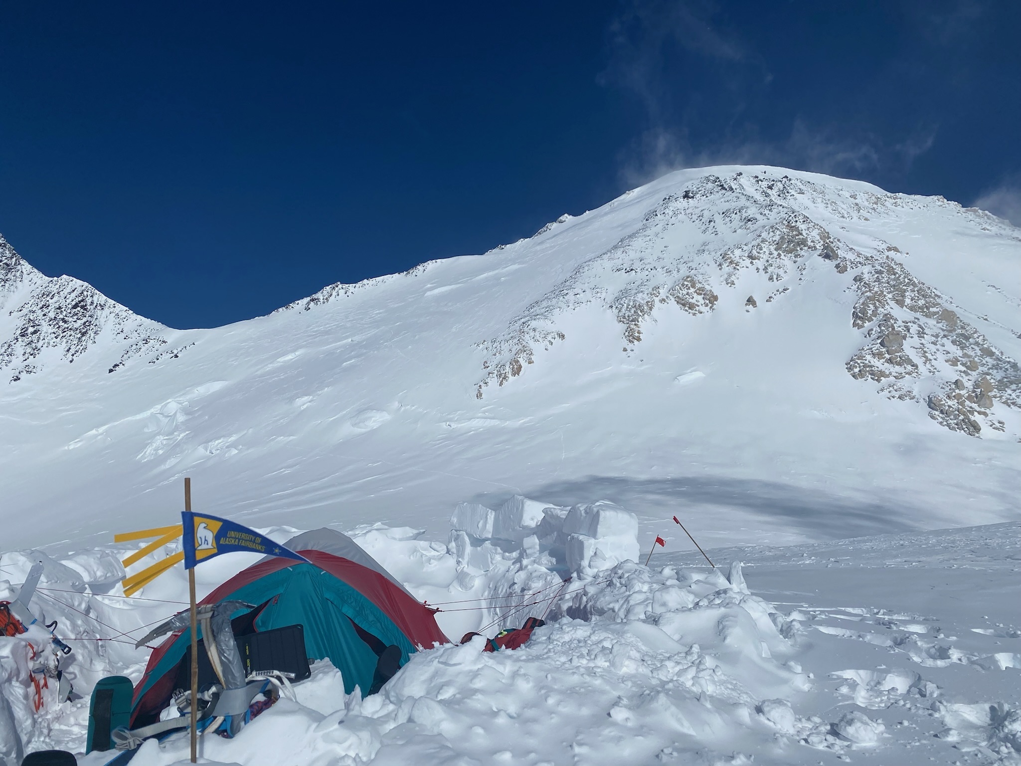 A tent sits in an excavated pit in the snow on a mountainside.