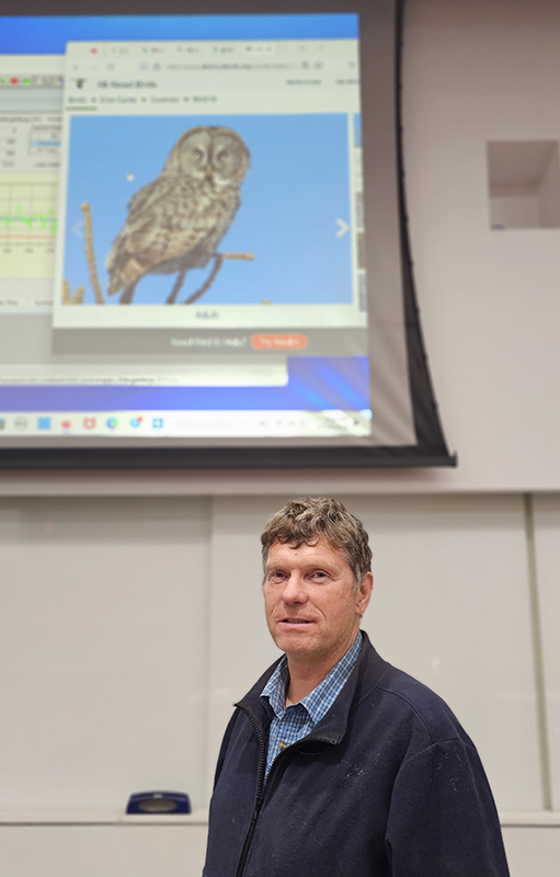 Man stands in front of projected image of a great gray owl.