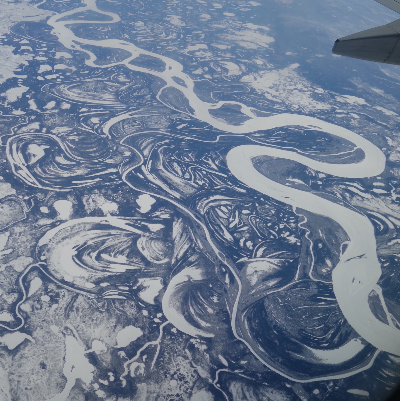 In an aerial photo, a large snow-covered frozen river and its associated sloughs wind through a flatland of spruce forest marked with willow-covered sandbars, sedge swamps, ponds and oxbow lakes.