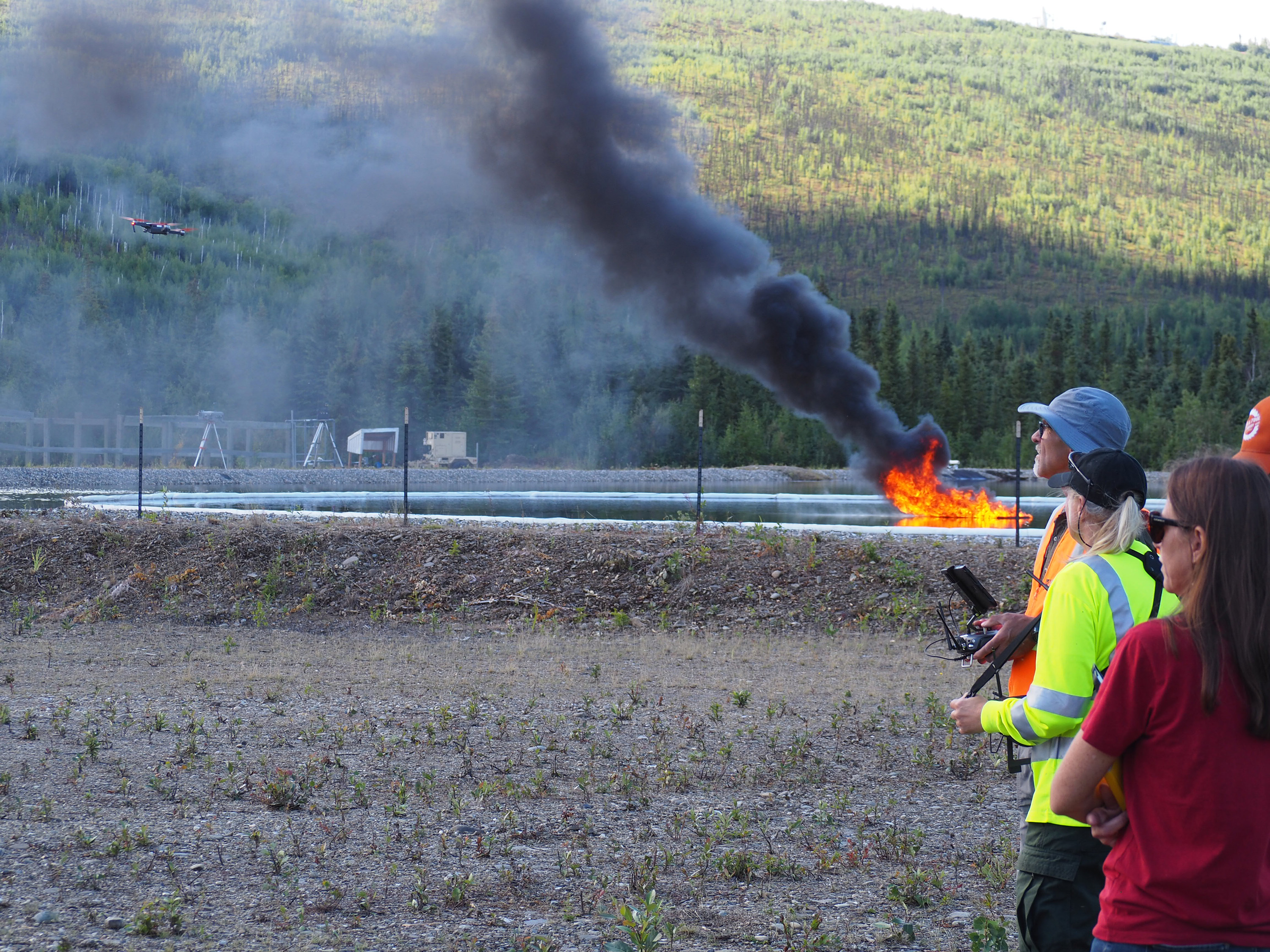 Drone pilots fly a drone over a burning oil spill during a test exercise.