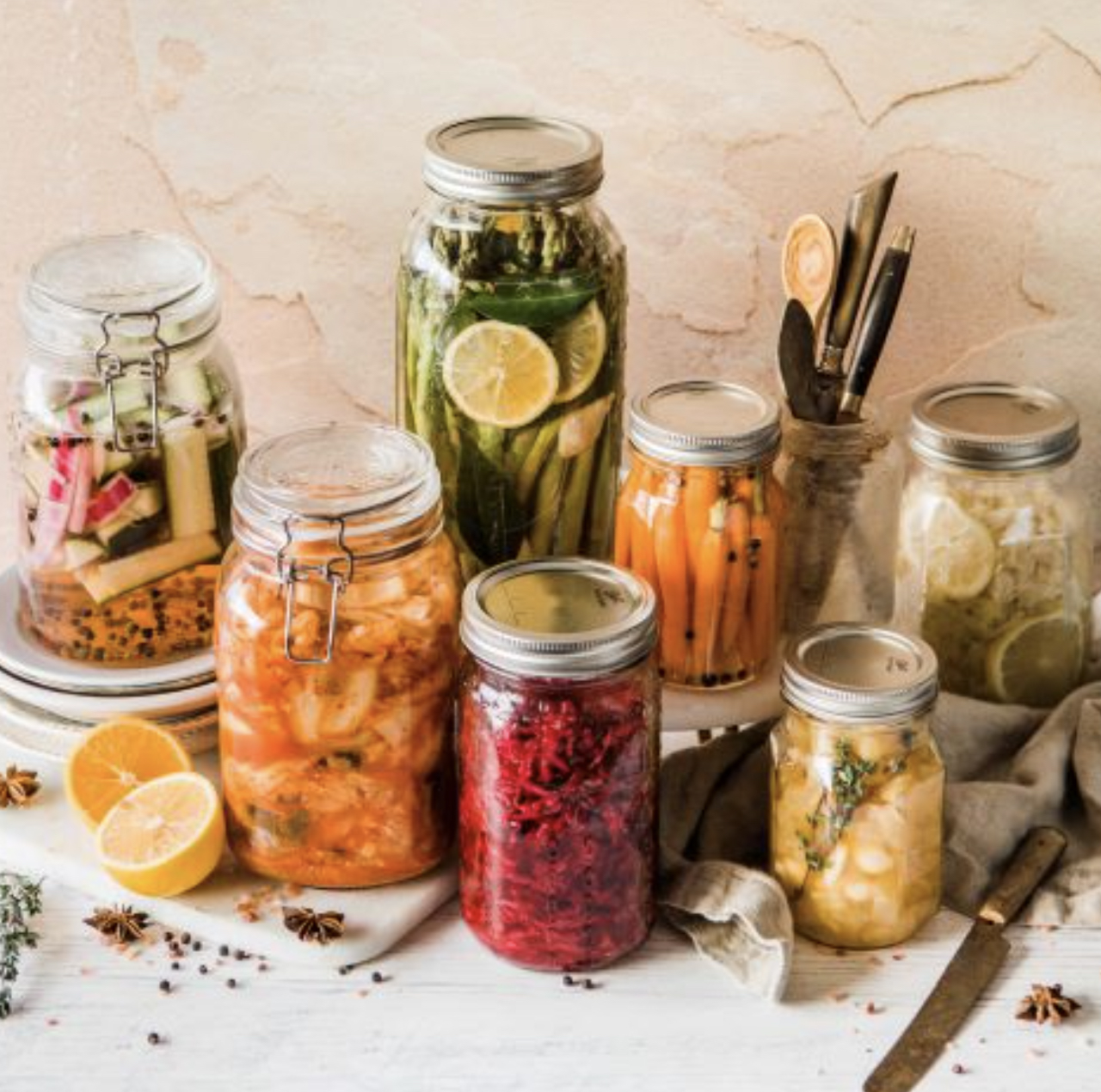 Jars of preserved vegetables sit on a table.