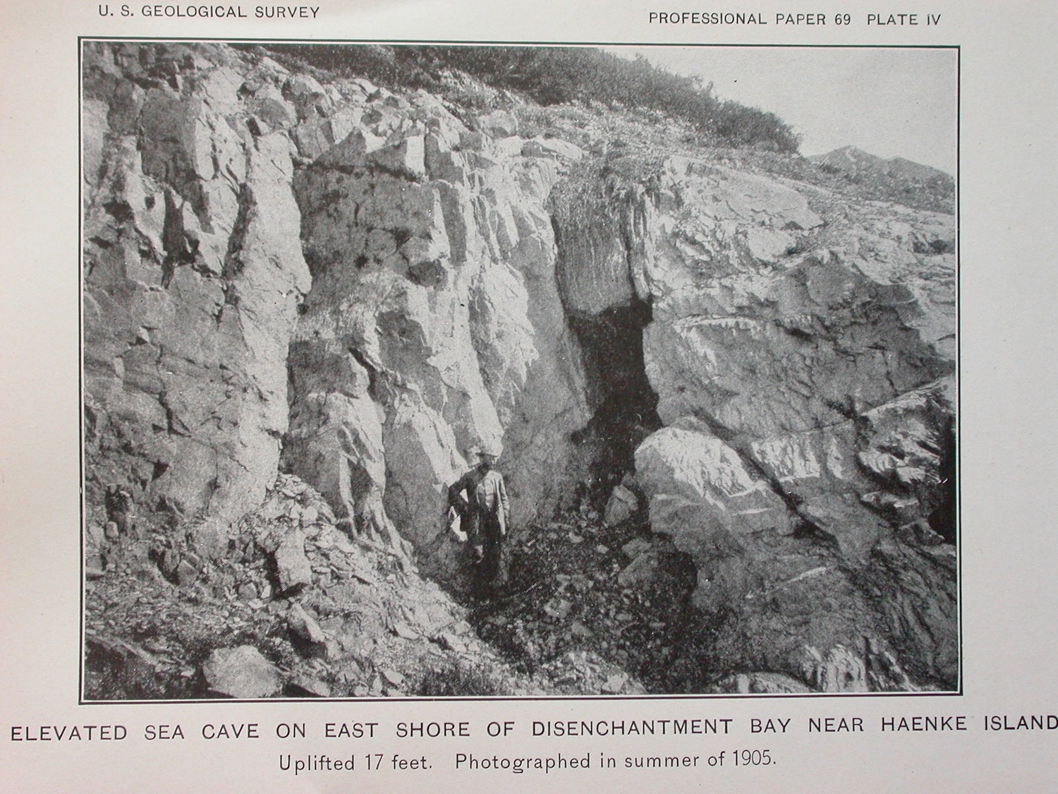 An old black-and-white photograph in a book shows a man standing next to a cave in rocks.