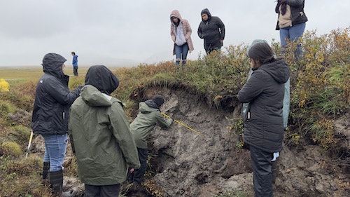 A group of students stand on a mound of permafrost.
