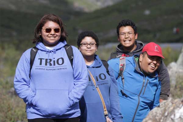 A group of students with TRIO shirts walk outdoors