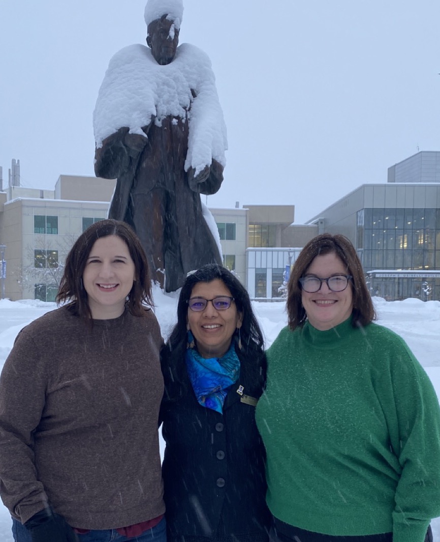 Michelle Strickland, former accreditation coordinator; Anupma Prakash, provost and executive vice chancellor; and Alex Fitts, vice provost and accreditation liaison officer pose in front of the snow covered statue of Charles Bunnell.