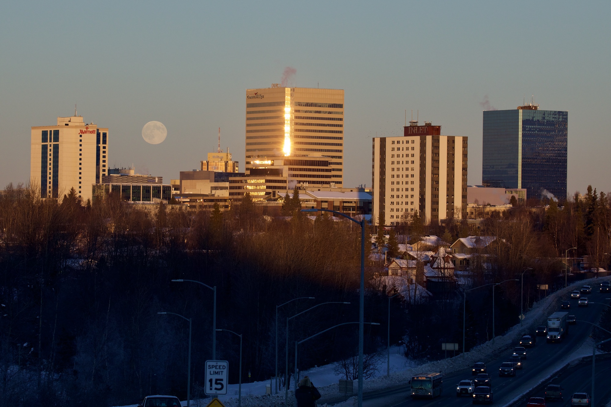 The moon rises above a collection of tall buildings.