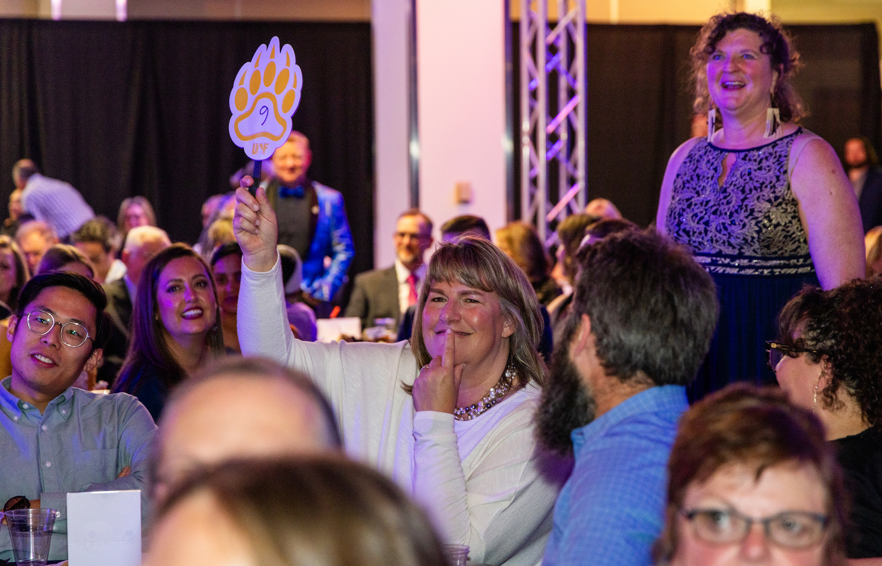 a woman holds a bidders paddle in a crowd of people