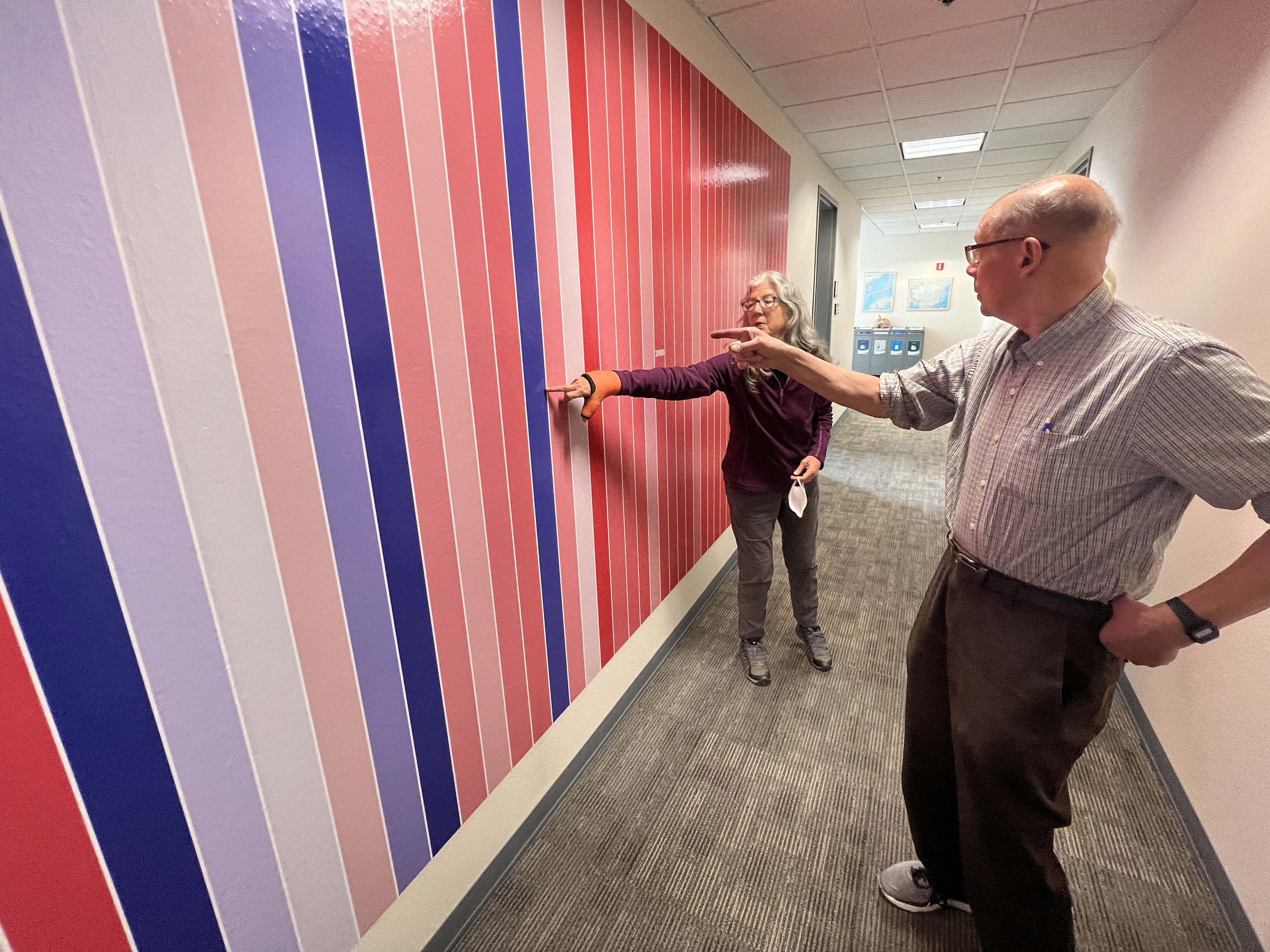 People point at a blue stripe on the climate stripe wall. 