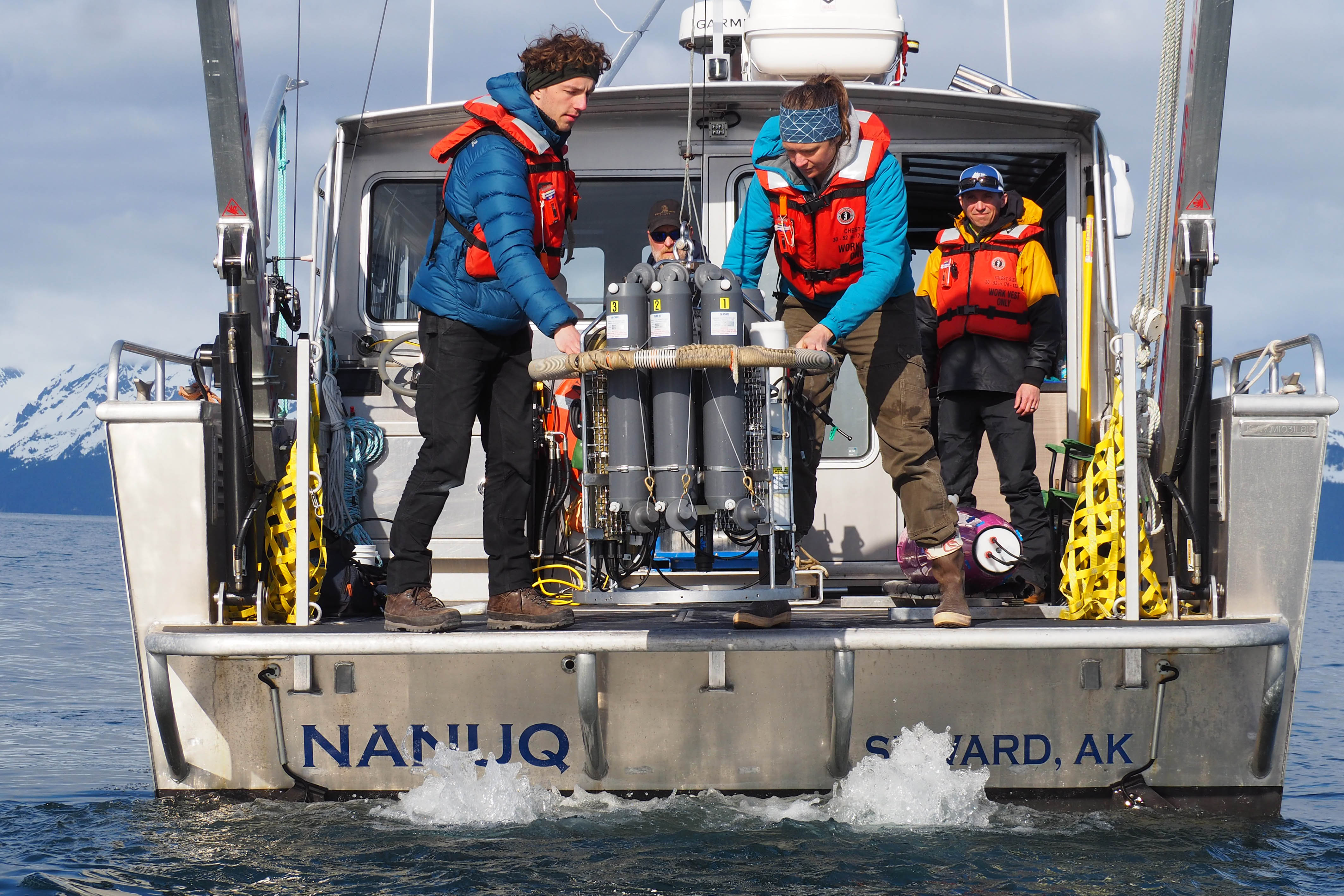 People on boat lowering metal equipment into ocean