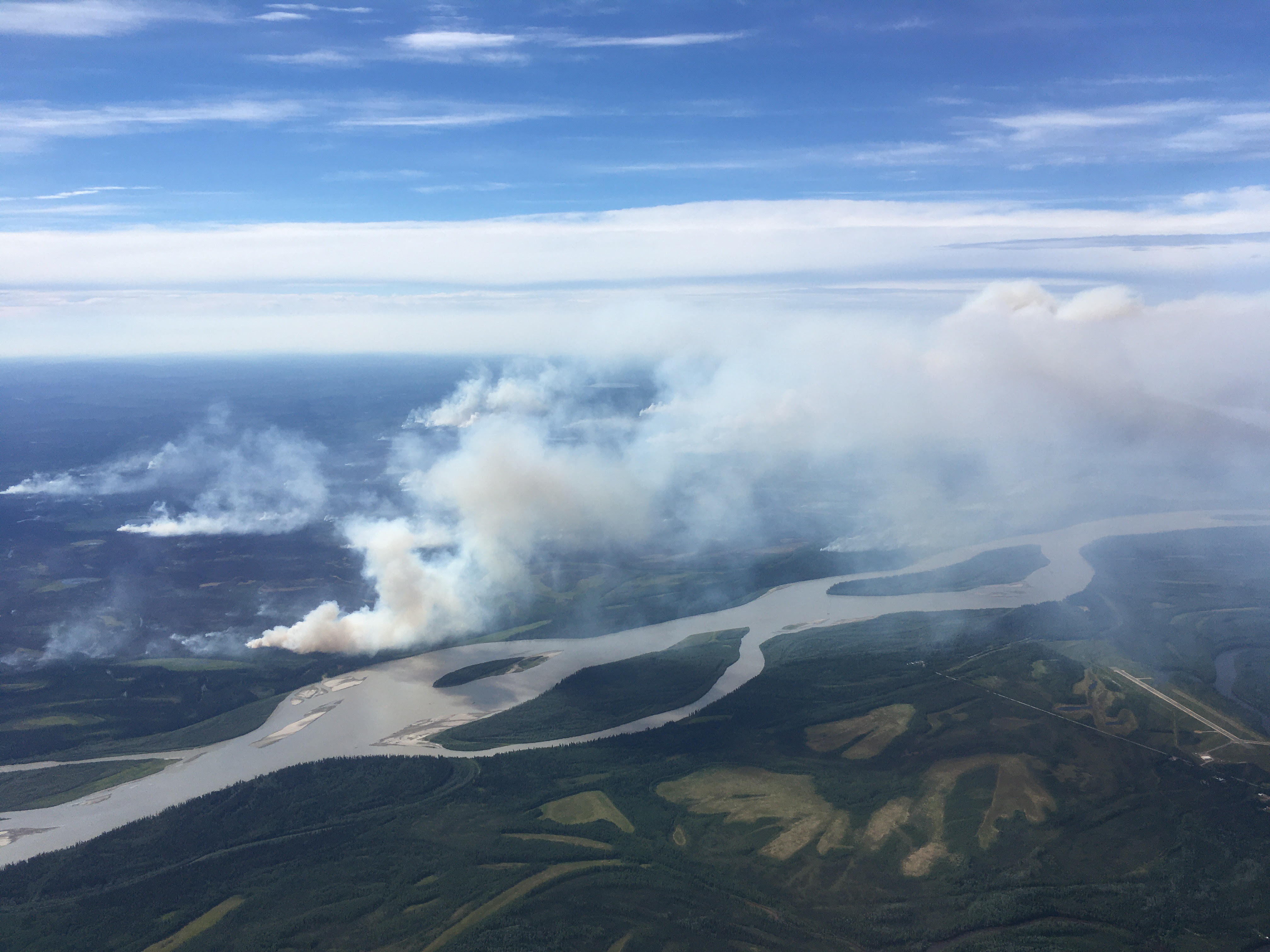 an aerial photo of a smoking wildfire with a river in the foreground