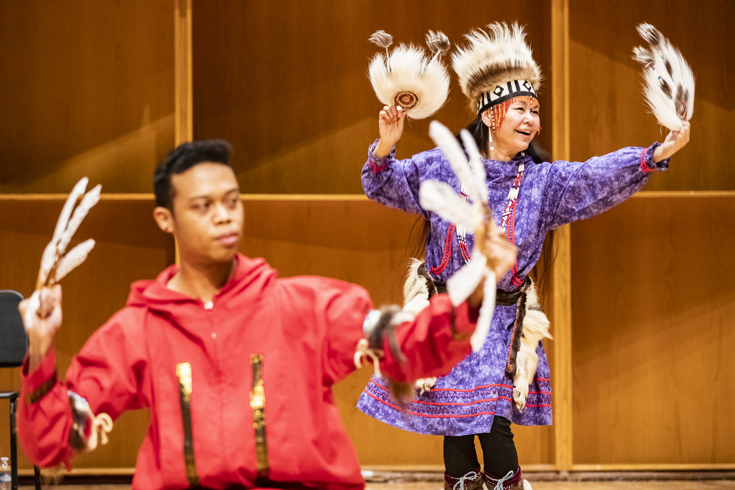 Two Yup'ik dancers dressed in regalia with fans performing onstage.