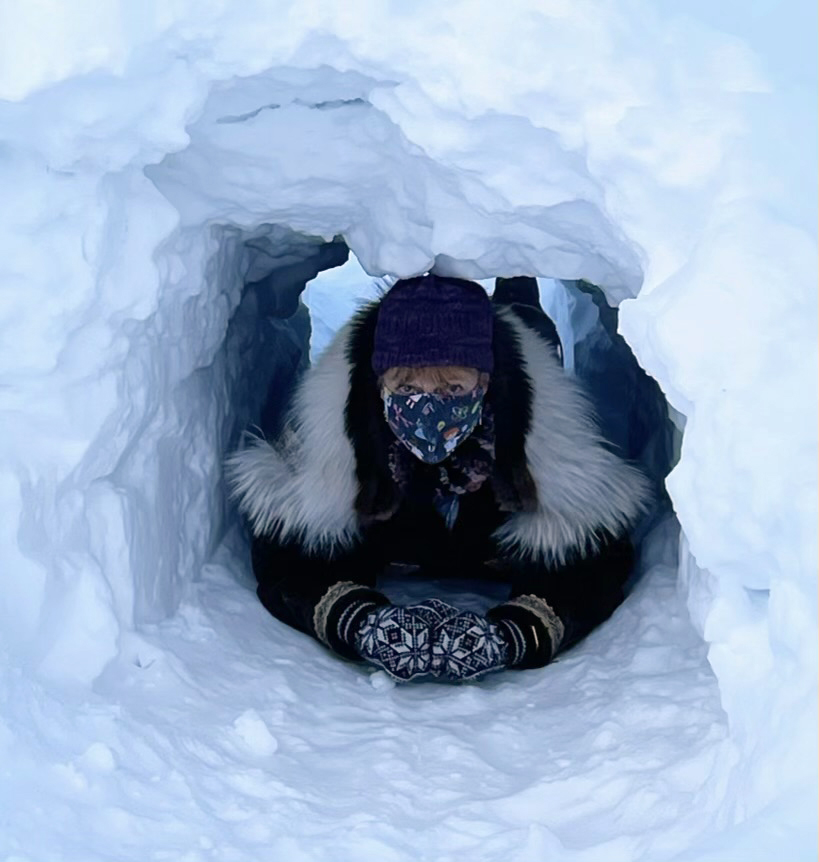 a woman in a parka peeking through a snow tunnel