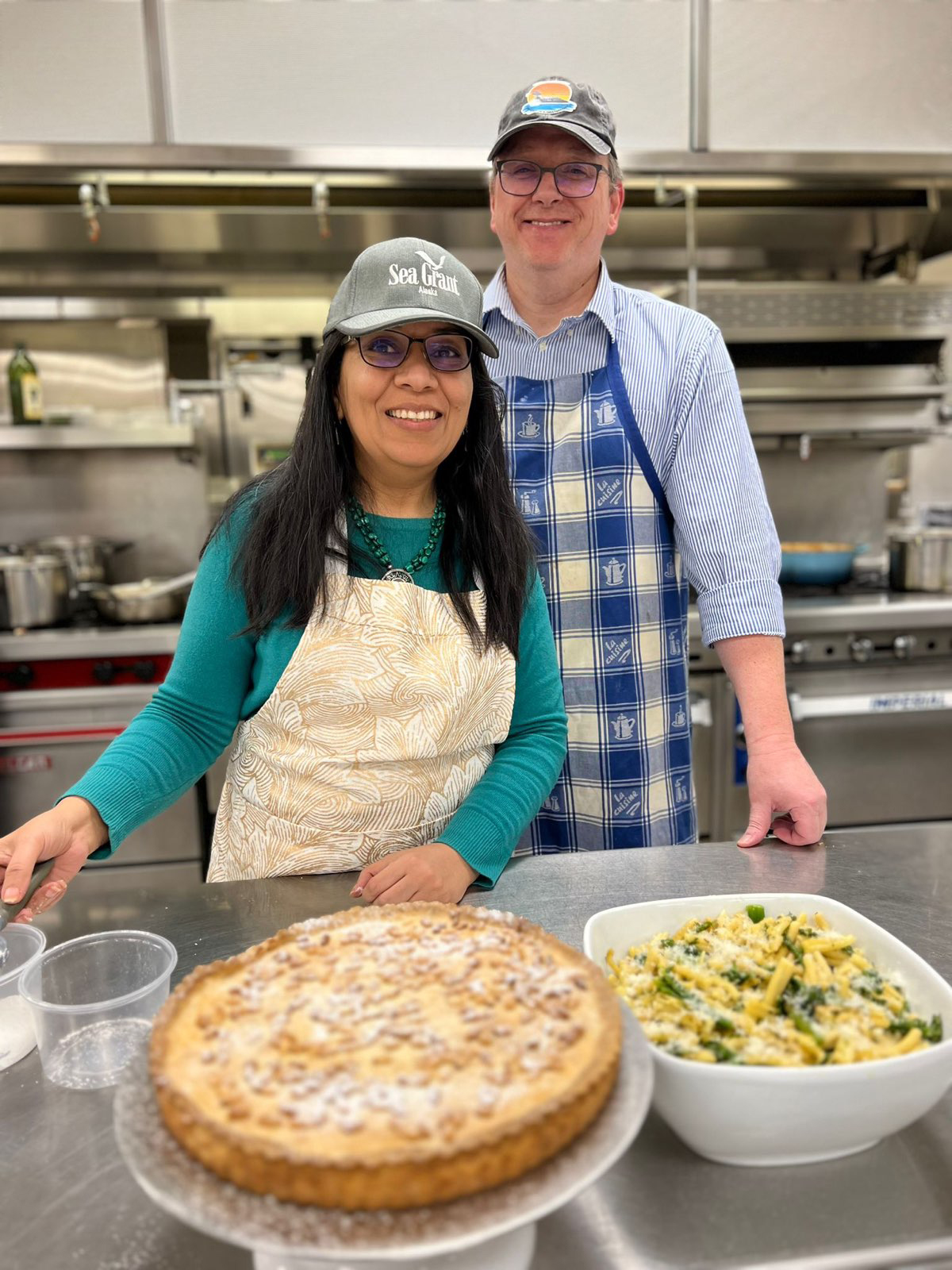 A man and woman take a break from cooking for a photo in a kitchen.