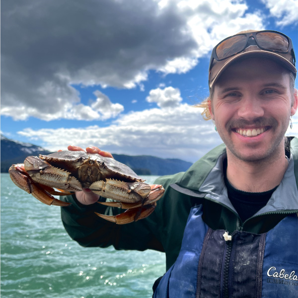 Graduate student Carter Johnson holds a Dungeness crab up for the camera while out in the field.