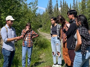 Muscarella (far left) explaining the role of bacteria in natural ecosystems to 2022 Rural Alaska Honors Institute students while in a boreal forest.