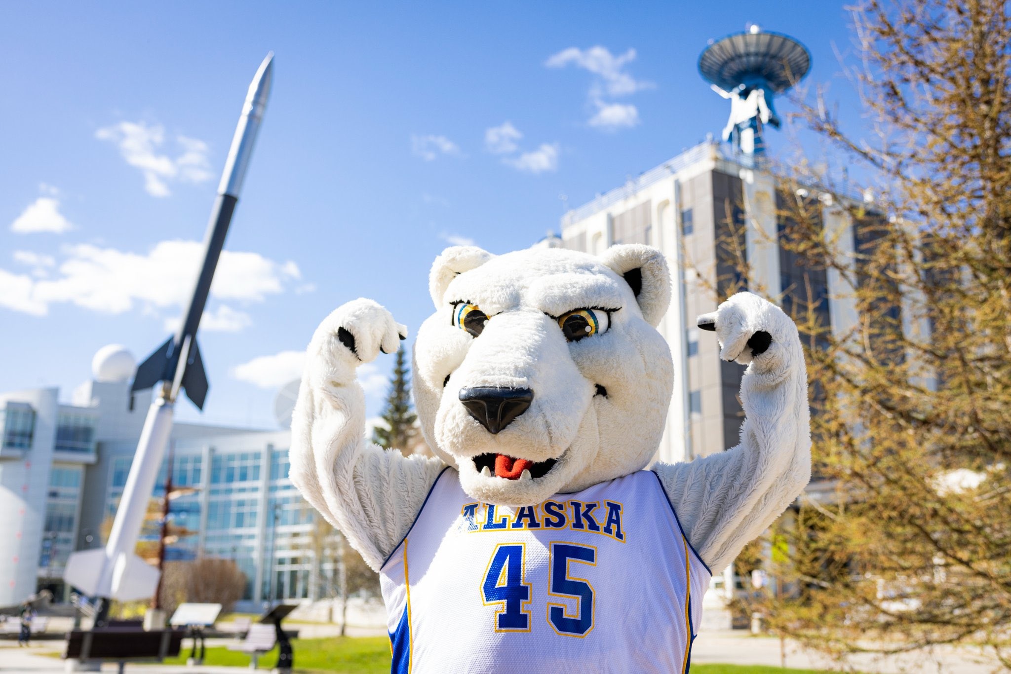 polar bear mascot in front of a rocket and some buildings
