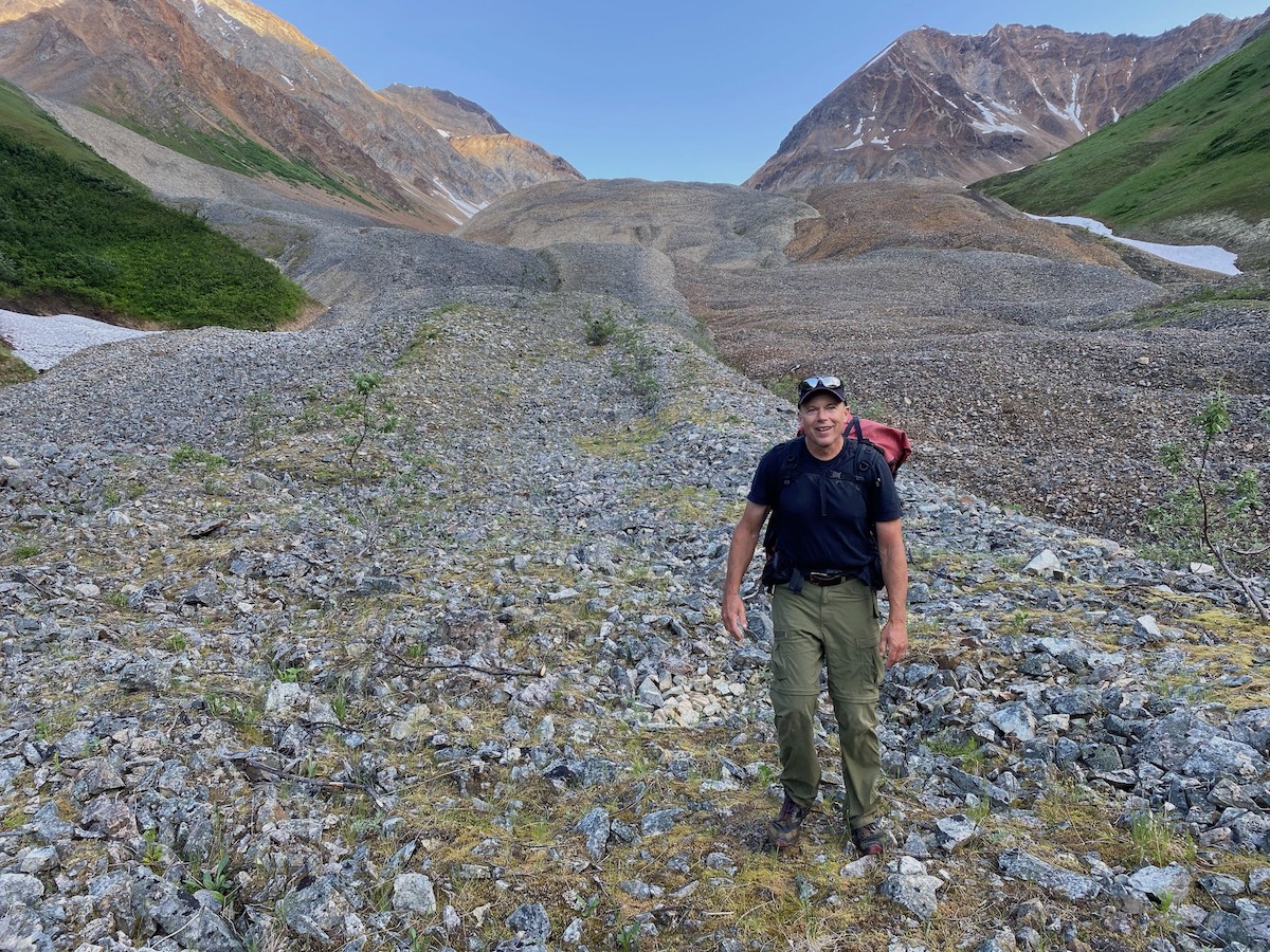 A man walks on a slope of mounded rocks in a mountain valley.