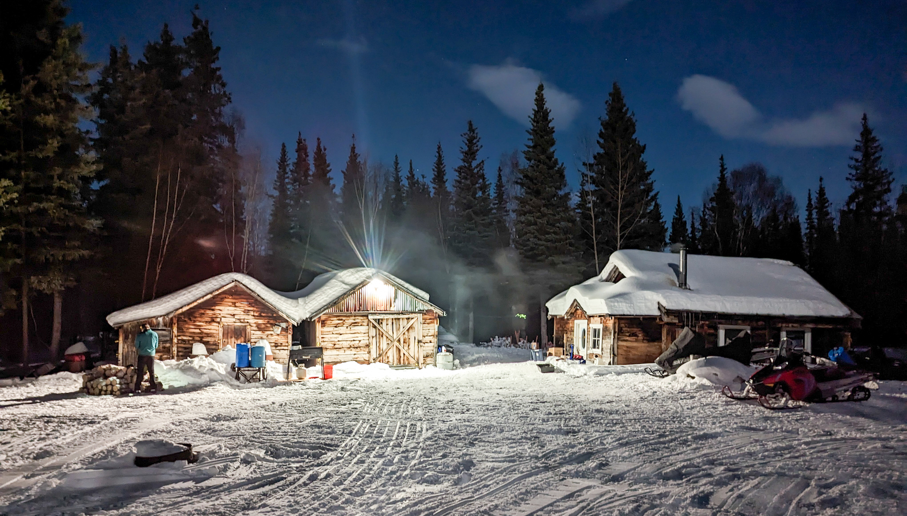 A light illuminates a set of snow-covered cabins at night.