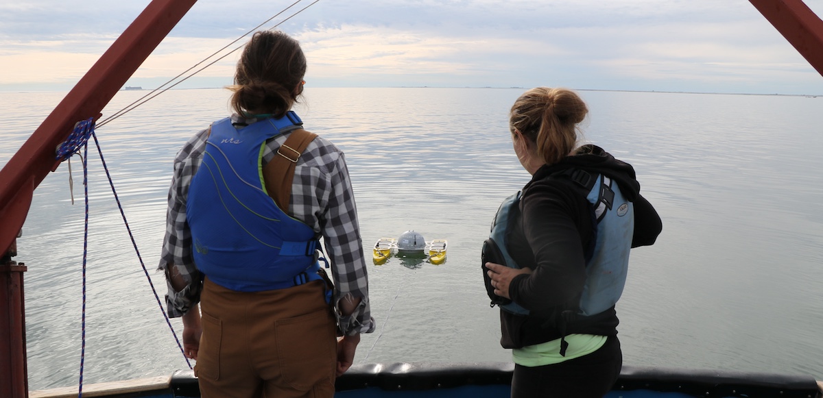 Researchers on the deck of a research vessel observe the deployment of a drone out at sea.