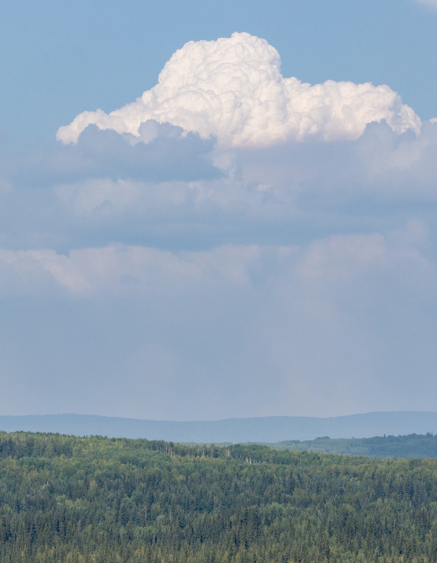 A white cumulus cloud rises above smoke and green hills.